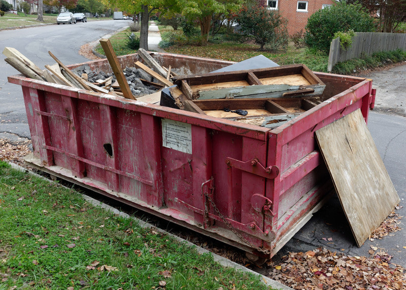 Red dumpster is full of scrap wood and about ready to be pulled away.