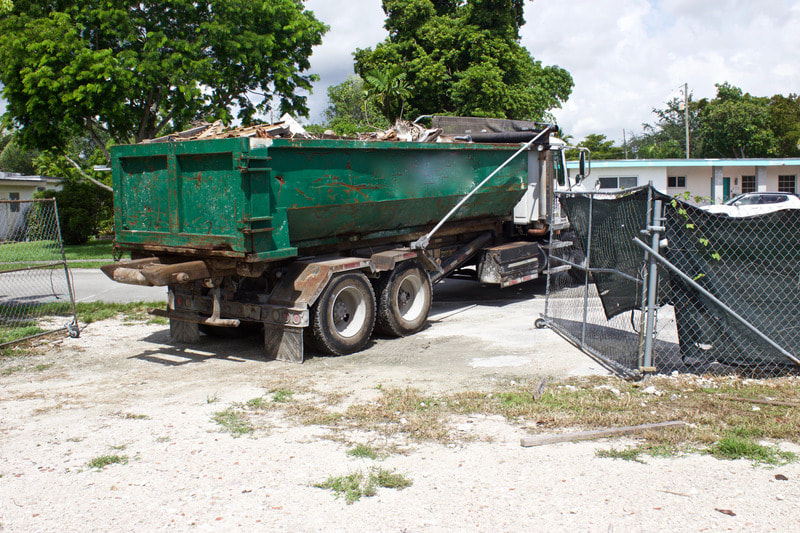 Green dumpster is being pulled away from a location by one of our trucks.